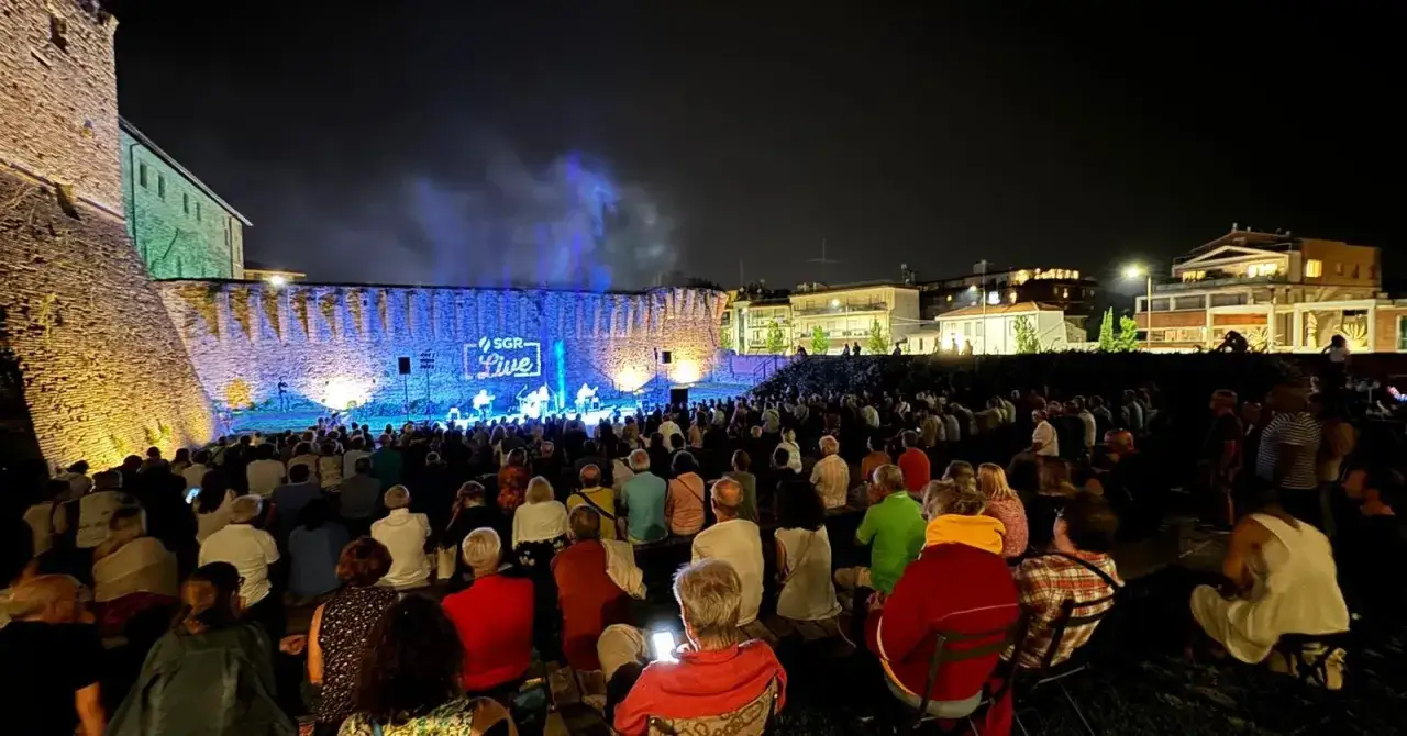 Concerto SGR Live sotto le mura illuminate di Rimini. Un pubblico numeroso assiste agli eventi serali.