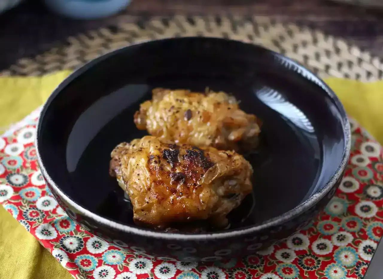Dwa chrupiące skrzydełka z kurczaka z airfryer, podane w czarnej misce na kolorowej serwetce.