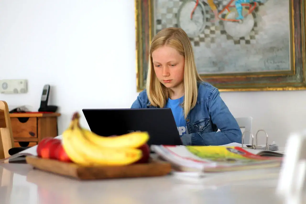 Ein Mädchen lernt konzentriert am Laptop, gestärkt durch ihre **Selbstwirksamkeit**. Obst liegt bereit für eine gesunde Pause.