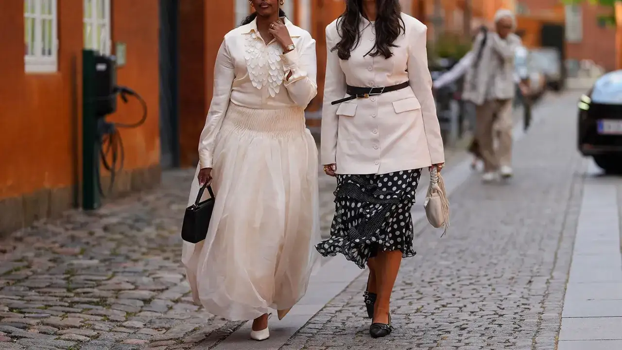 Zwei Frauen in eleganten Outfits, die den **musical dress code** interpretieren: eine in einem cremefarbenen Kleid, die andere in Blazer und Polka-Dot-Rock.