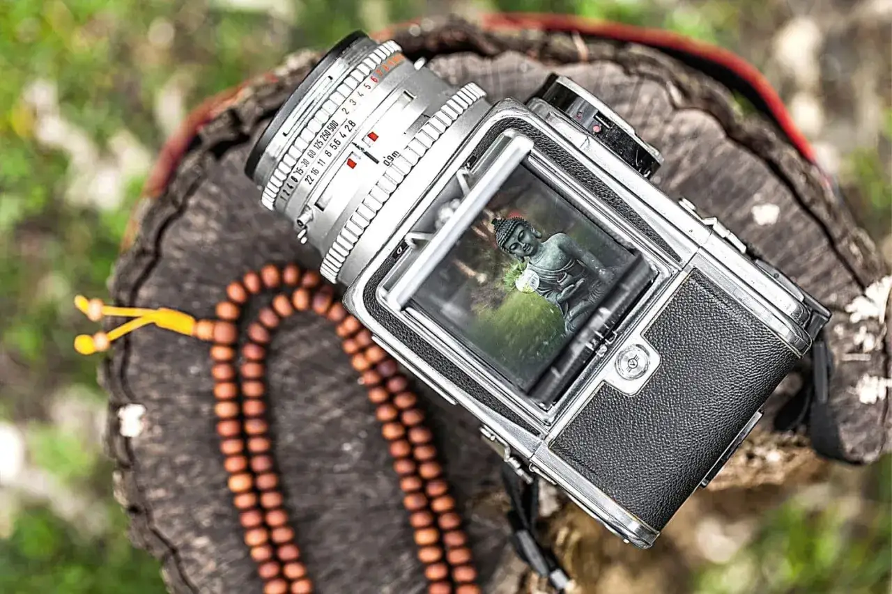 A vintage Hasselblad 500c camera rests on a wooden surface, its viewfinder reflecting a serene Buddha statue.