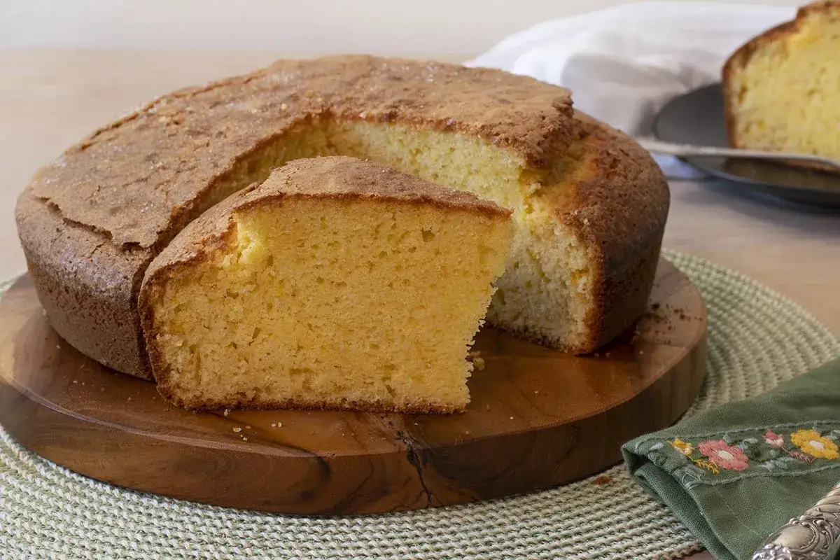 Un delicioso bizcocho de naranja, esponjoso y dorado, con una rebanada cortada para mostrar su interior.