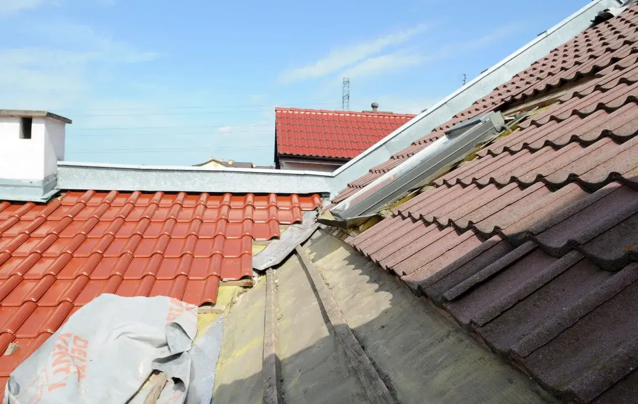 Dachówki ceramiczne i stare pokrycie dachowe, być może eternit, z widocznym oknem dachowym.