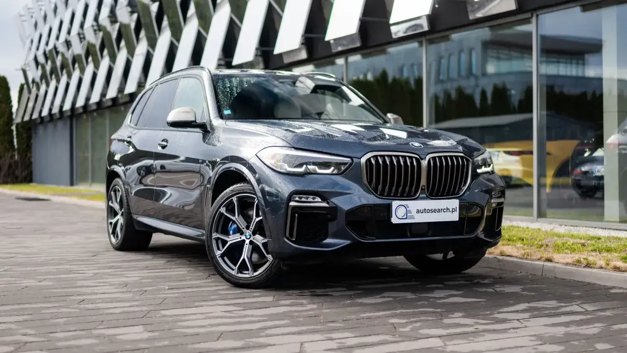 BMW X5 M50d w ciemnoszarym kolorze, zaparkowany przed nowoczesnym budynkiem.