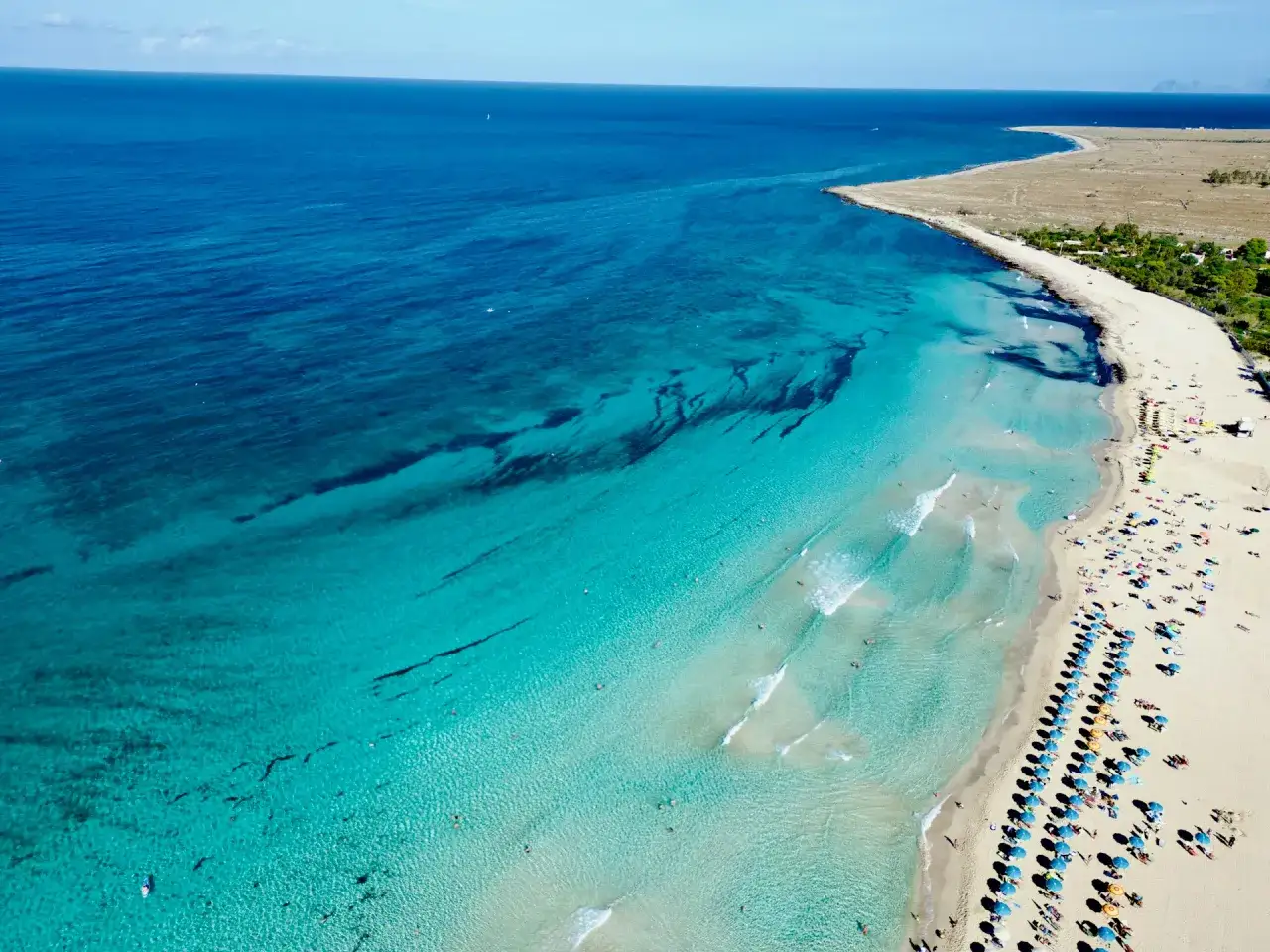 Un incantevole **sizilien strand** con acque cristalline e sabbia dorata, bagnato da un mare turchese. Ombrelloni colorati e bagnanti godono del sole.