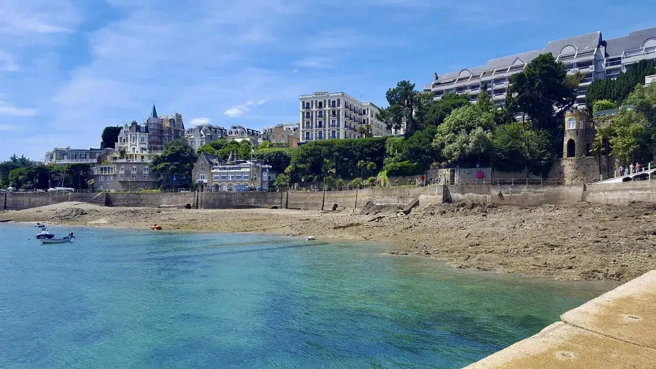 Vue sur la côte rocheuse et la mer turquoise, avec des bâtiments imposants en arrière-plan, typiques du pays malouin.