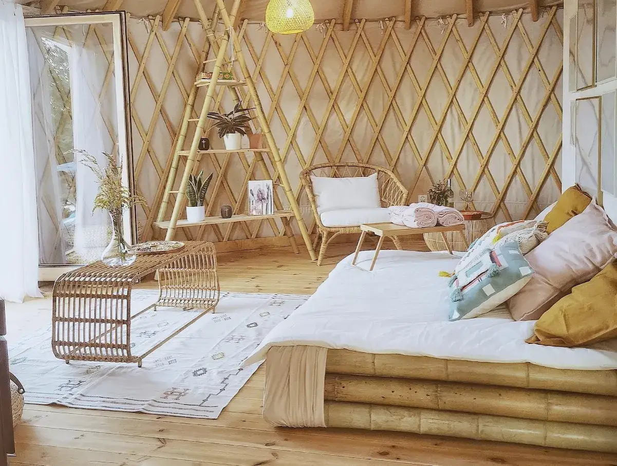Gem&uuml;tliche Jurte als Wohnhaus mit Bett, Rattantisch und Regal. Nat&uuml;rliche Materialien schaffen eine entspannte Atmosph&auml;re.