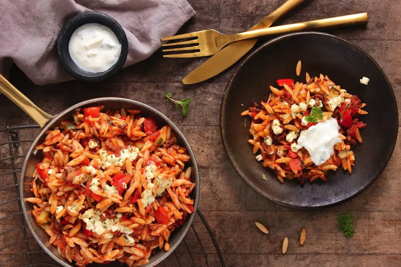 Zwei Portionen Kritharaki-Rezept mit Hackfleisch, Tomaten und Feta, serviert mit Joghurt-Dip.