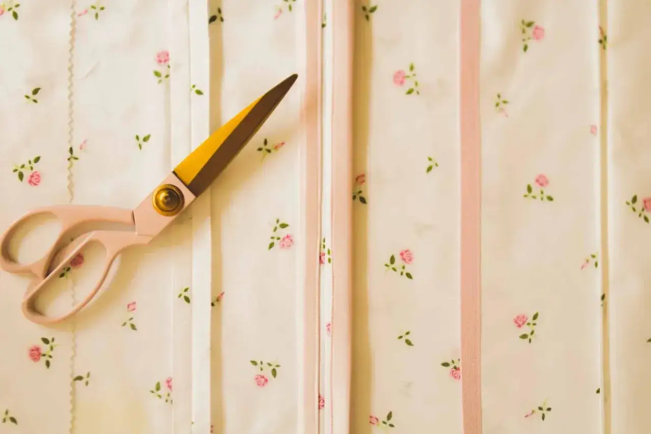Ciseaux roses sur un tissu &agrave; petites fleurs roses. La lisi&egrave;re du tissu est visible, avec des rubans roses et blancs.
