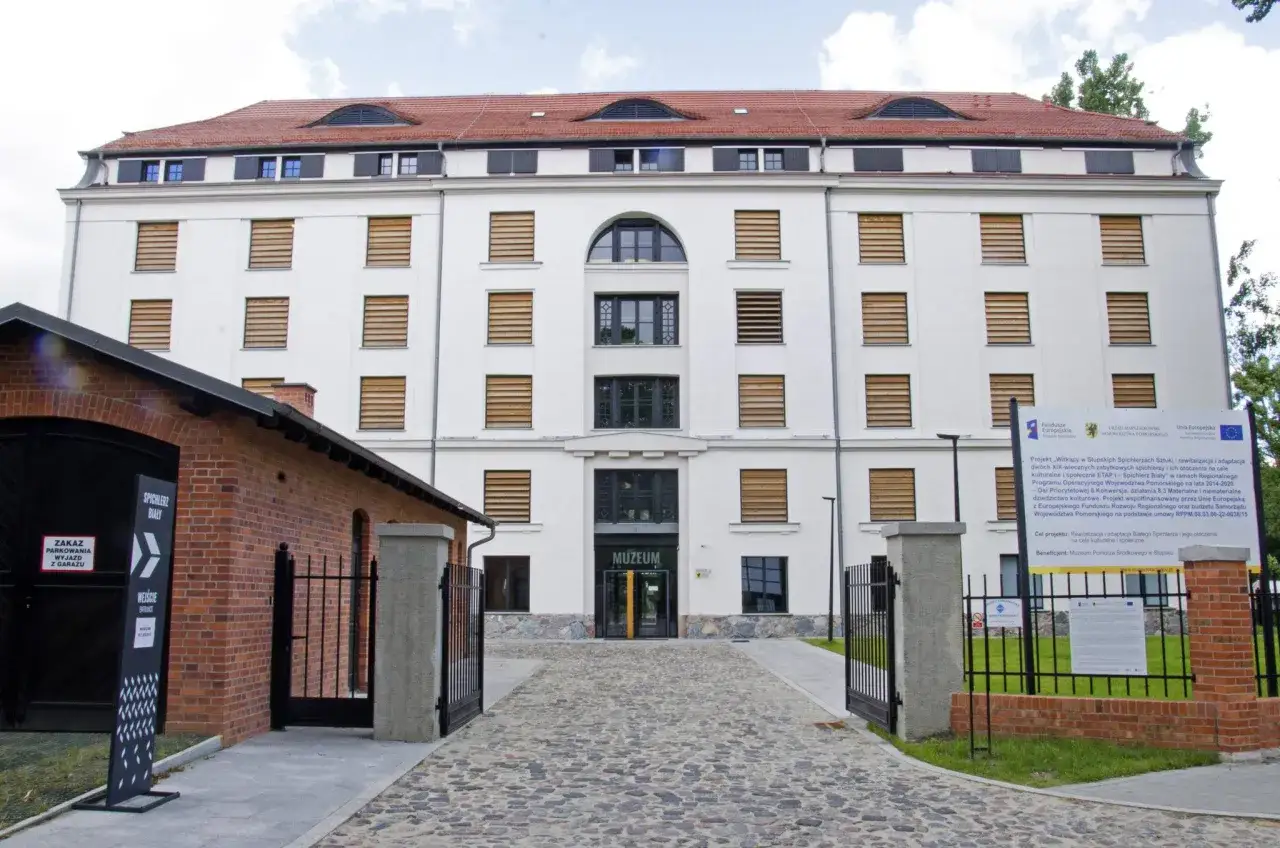 Biały spichlerz w Słupsku, obecnie muzeum, z ceglanym budynkiem obok.