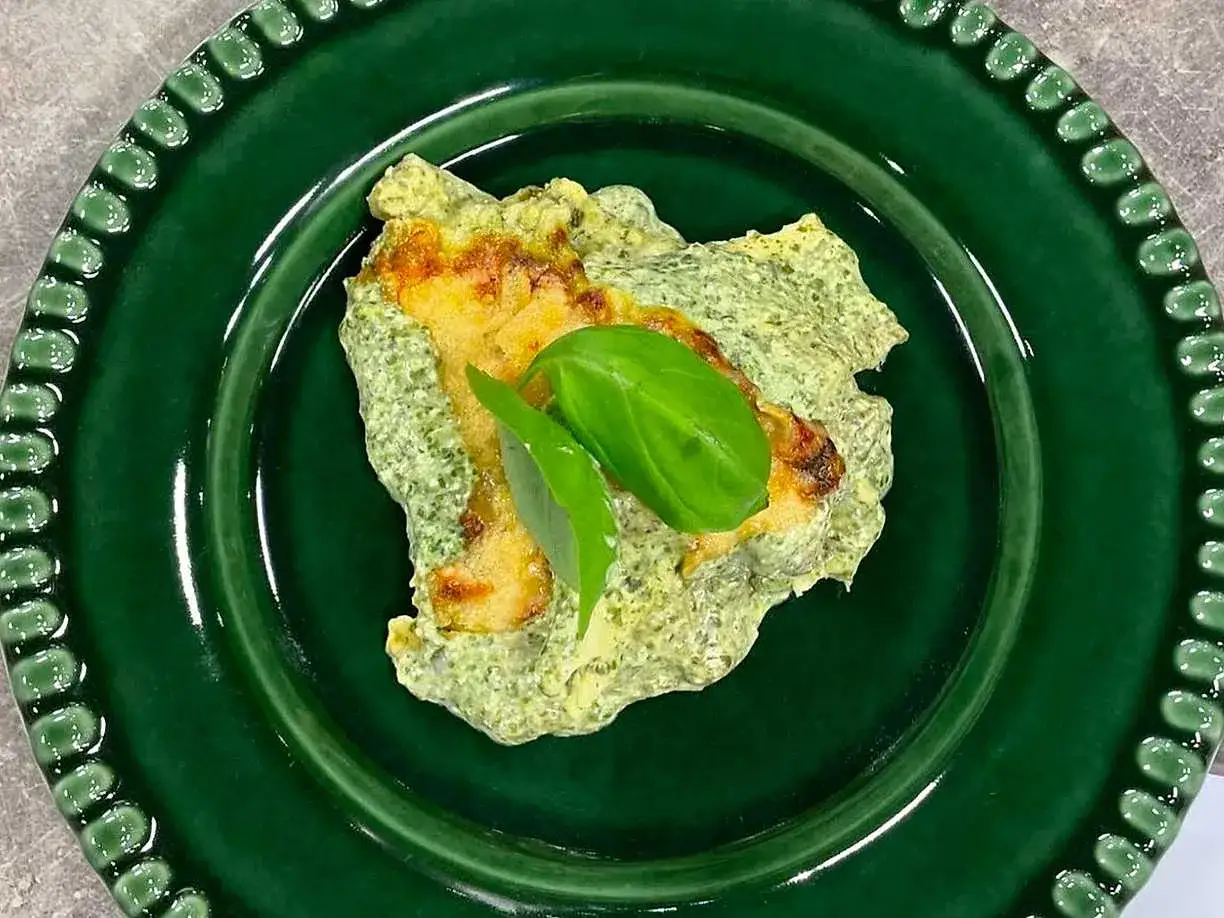 En portion lasagne med zucchini och fetaost, toppad med f&auml;rsk basilika, serveras p&aring; en gr&ouml;n tallrik.