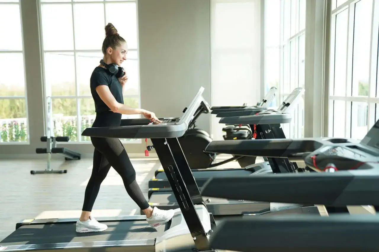 Frau mit Kopfhörern genießt ihr **walken auf dem Laufband** in einem hellen Fitnessstudio.