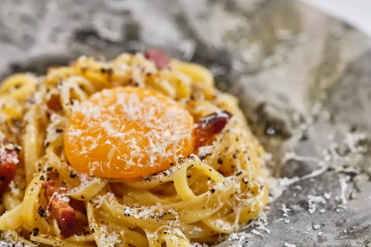 Pasta con huevo crudo, queso rallado y trozos de tocino. Un plato de salsa carbonara listo para mezclar y disfrutar.
