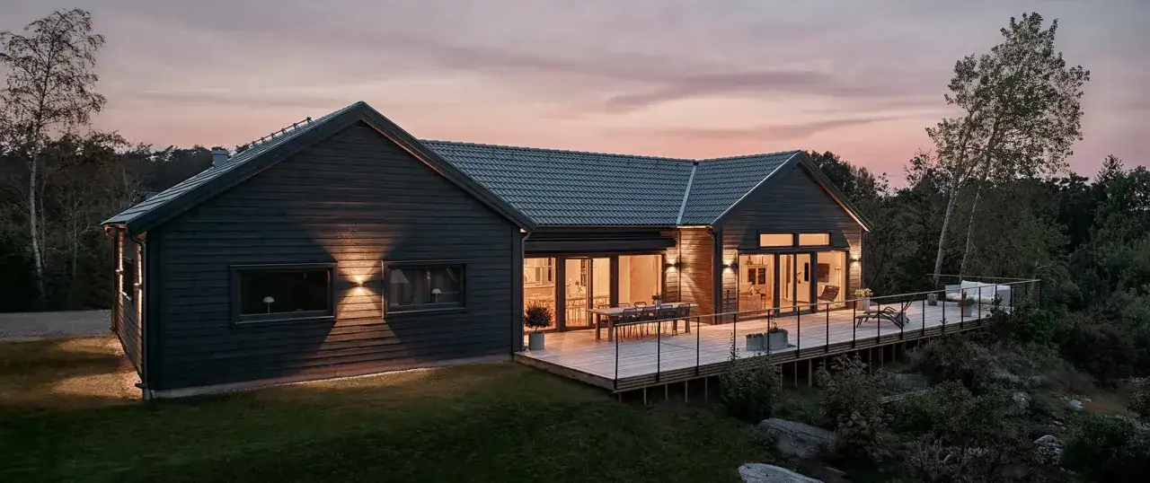 Mörkt trähus med stor altan i kvällsljus. Perfekt utbyggnad hus inspiration för ett modernt hem i naturen.
