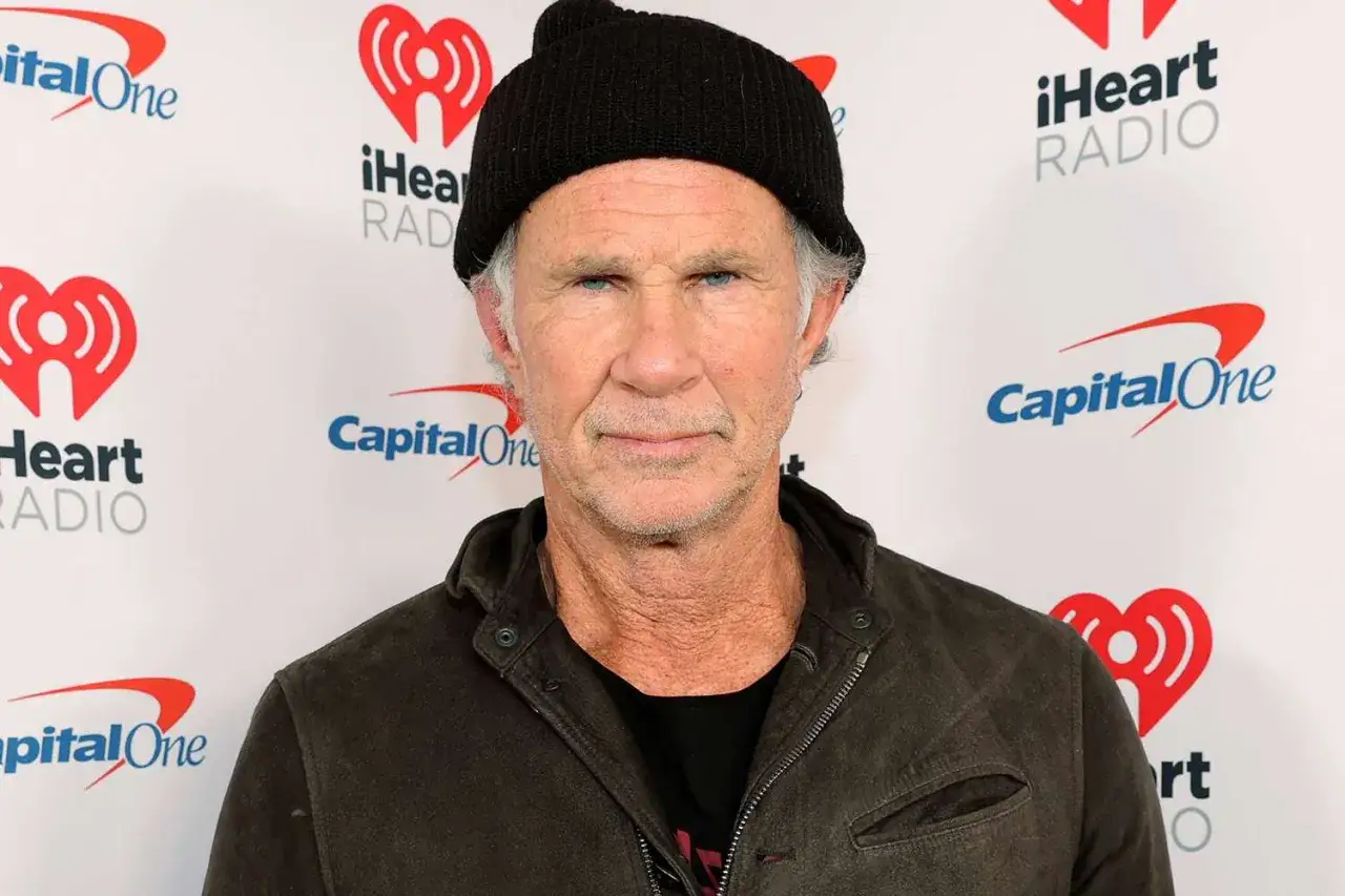 Chad Smith, perkusista Red Hot Chili Peppers, w czarnej czapce i kurtce, na tle logo iHeart Radio i Capital One.