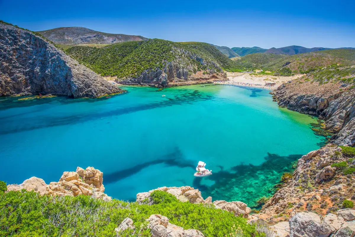 La splendida **Buggerru spiaggia** incanta con acque turchesi e rocce scoscese. Una barca solca il mare cristallino, mentre la sabbia dorata invita al relax.