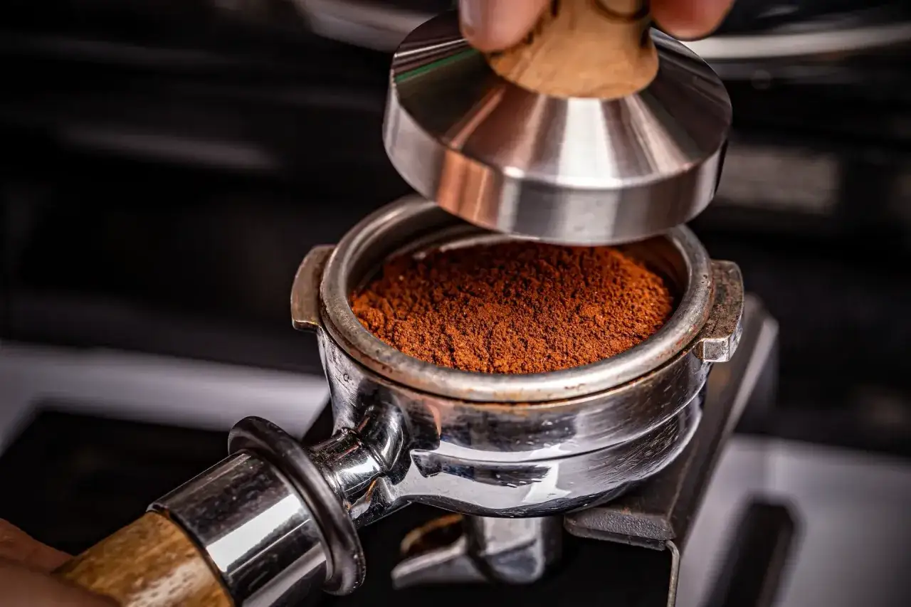 Hand presst Kaffeepulver im Siebtr&auml;ger, um manuell Espresso zuzubereiten.