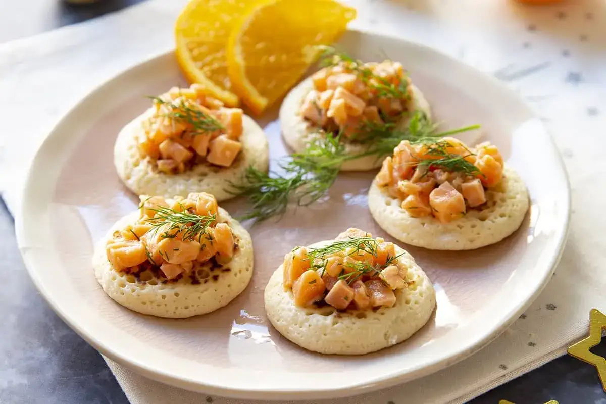 Cinq blinis garnis de tartare de saumon frais et d'aneth, accompagn&eacute;s de quartiers d'orange. Une garniture l&eacute;g&egrave;re et savoureuse.