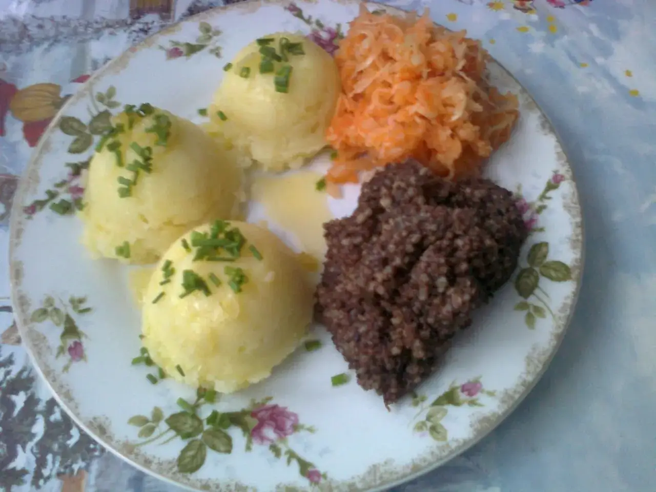Kaszanka po śląsku z puree ziemniaczanym i surówką z marchewki na talerzu z kwiatowym wzorem.