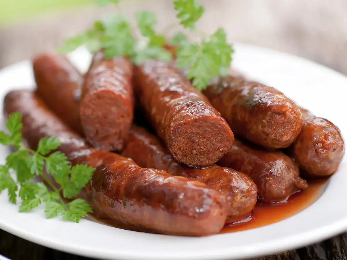 Des merguez au four, dor&eacute;es et juteuses, servies sur une assiette blanche avec une touche de persil frais. Un d&eacute;lice &agrave; partager.