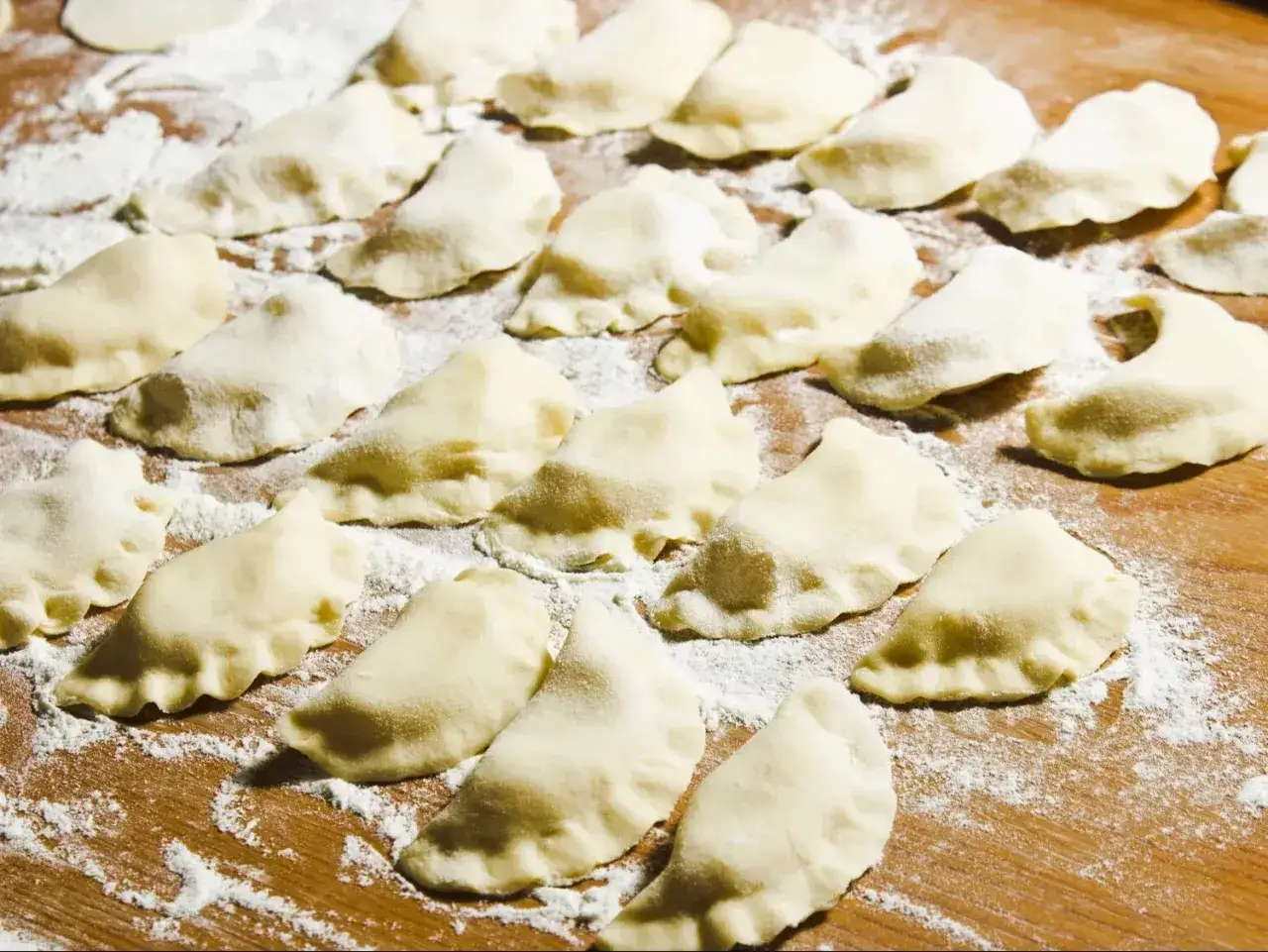 Gotowe do gotowania pierogi z serem, jak z przepisu Magdy Gessler, ułożone na drewnianej desce oprószonej mąką.