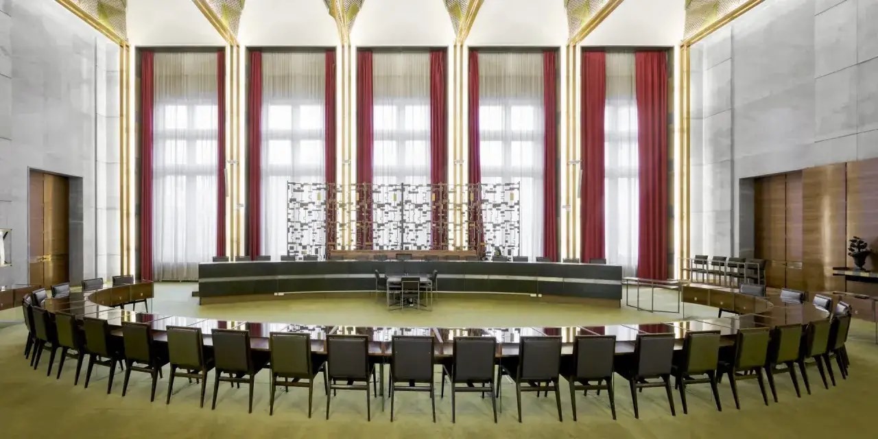 Salle de conf&eacute;rence majestueuse avec une grande table ovale, des si&egrave;ges en cuir et des rideaux rouges. Un d&eacute;cor d'&eacute;poque, peut-&ecirc;tre pour une r&eacute;union de **Maxime Old**.