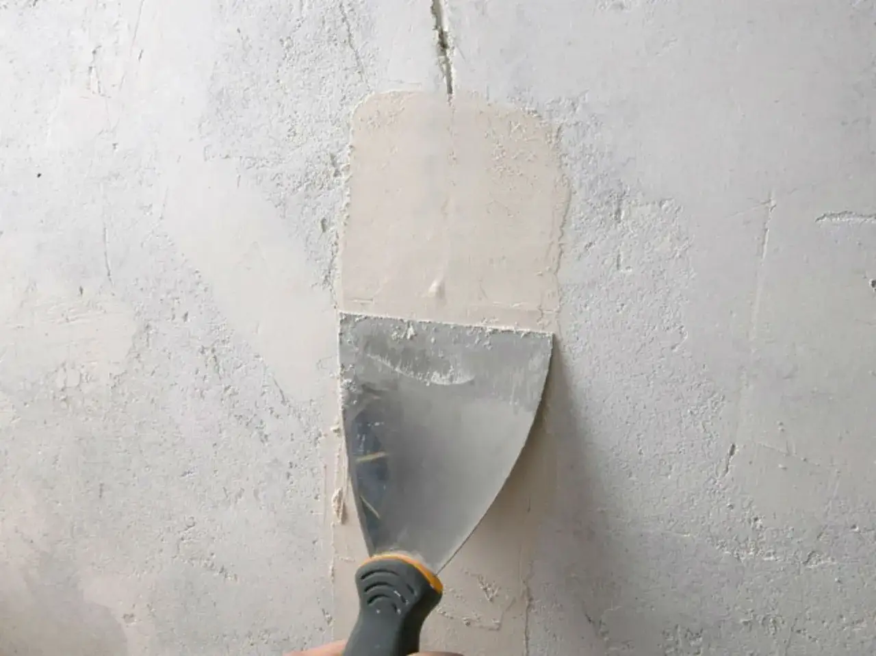 Application d'enduit pour réparer grosse fissure mur intérieur. Une spatule lisse la surface.