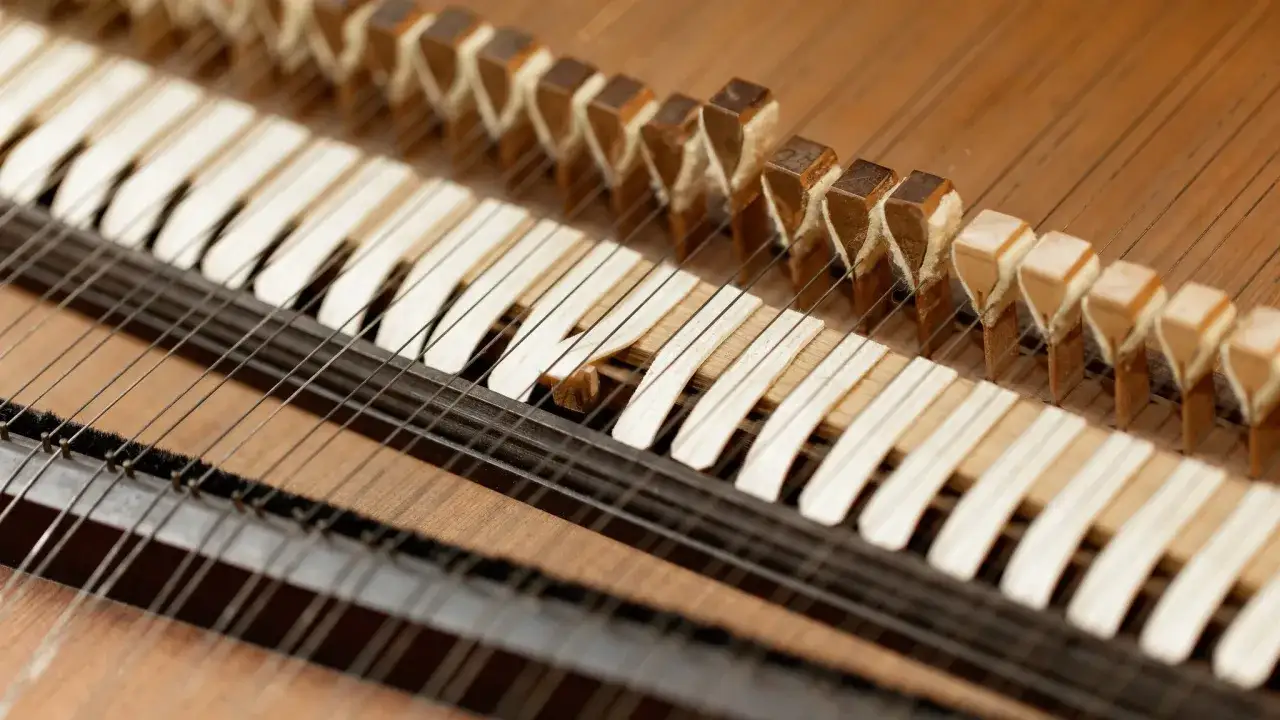 Zbliżenie na mechanizm klawesynu instrumentu: drewniane klawisze i struny.