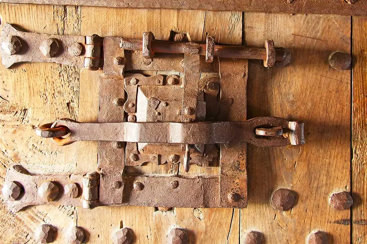 Parti di una serratura antica in ferro battuto su una porta di legno. Il meccanismo arrugginito mostra chiavistelli robusti e rivetti.