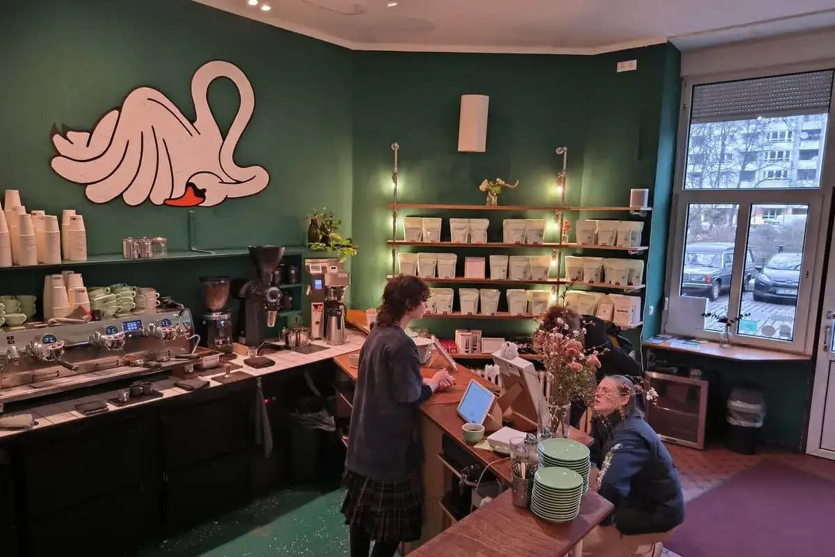 Un caff&egrave; accogliente a Berlino, con un'illustrazione di cigno stilizzato e scaffali pieni di pacchetti di caff&egrave;. Ottimo per scoprire cosa fare a Berlino.
