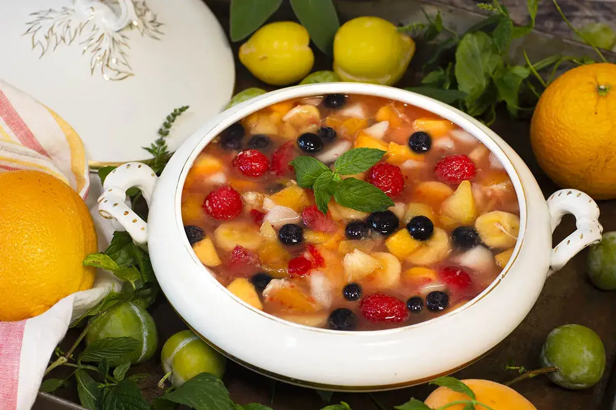 Deliciosa ensalada de frutas con fresas, arándanos, plátano y melocotón en un cuenco blanco.