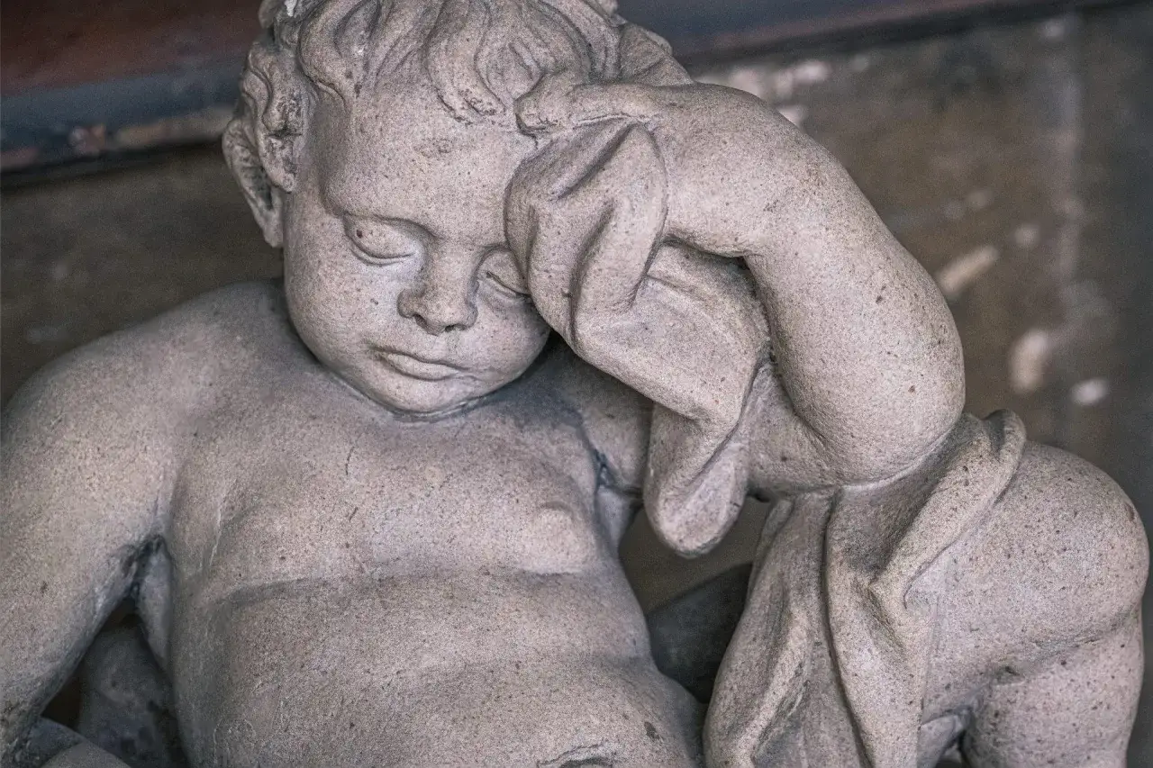 Kamienna rzeźba dziecka z zasłoniętą twarzą. Sen o śmierci własnego dziecka może symbolizować koniec pewnego etapu.
