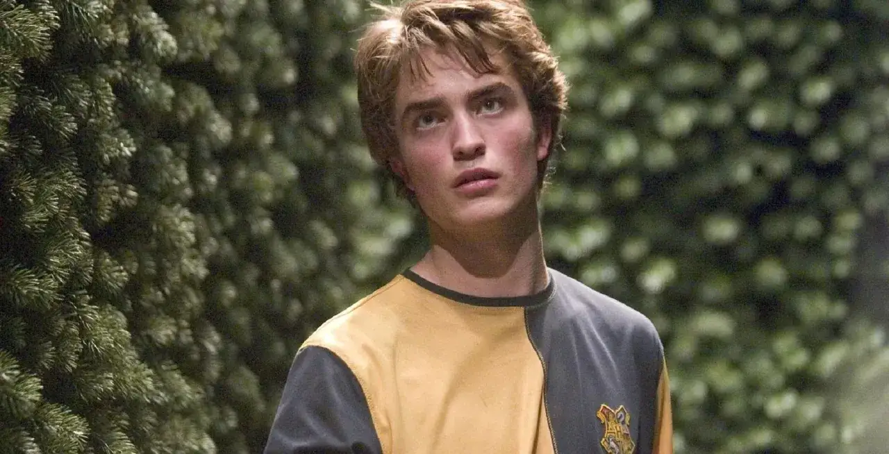 Cedrik Diggory, dumny reprezentant Hufflepuff, w swoim żółto-szarym swetrze, wygląda na zamyślonego wśród zieleni.