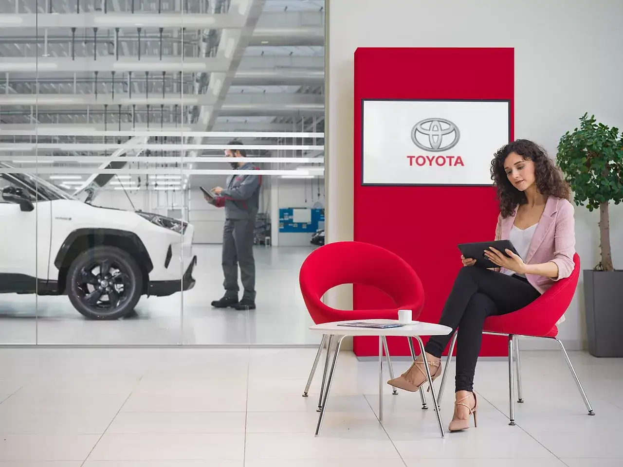 En kvinna v&auml;ntar i en bekv&auml;m lounge medan en tekniker inspekterar en bil. Allt under Toyotas trygga garanti.
