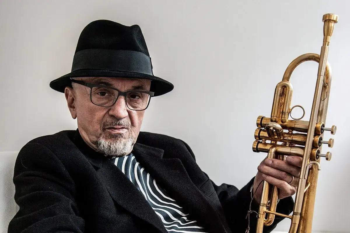 Tomasz Trębacz, kompozytor jazzowy, w czarnym kapeluszu i okularach, trzymający w dłoni złoty instrument dęty.
