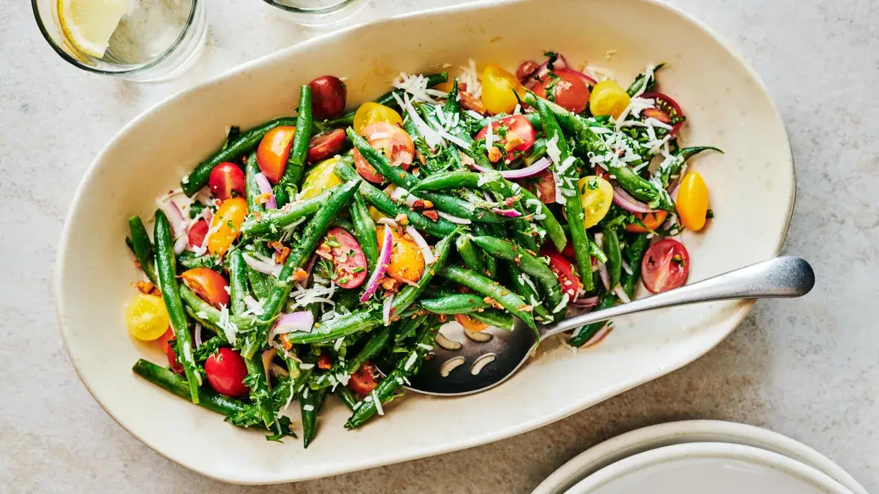 Salade color&eacute;e de haricots verts, tomates cerises, oignons rouges et feta r&acirc;p&eacute;e, servie dans un plat ovale avec une cuill&egrave;re.