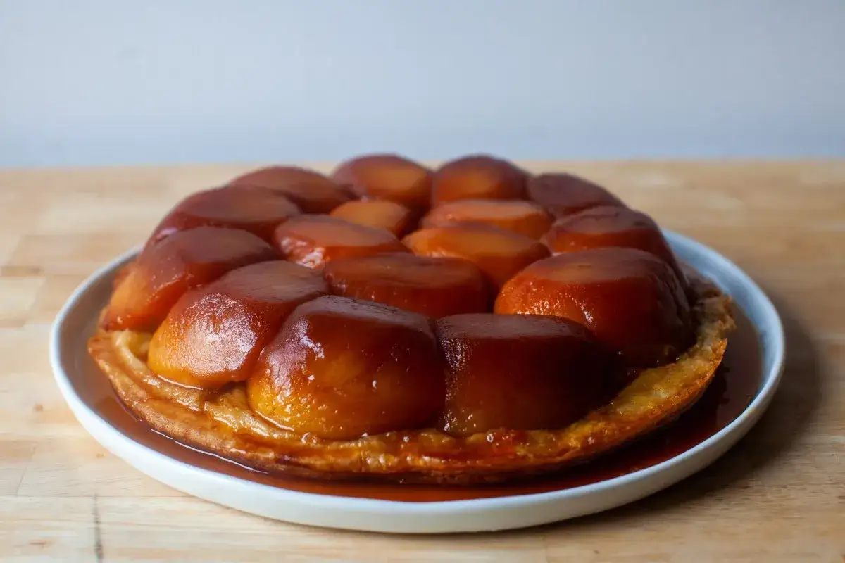 Eine gl&auml;nzende, karamellisierte Tarte Tatin original, mit &Auml;pfeln und knusprigem Teig, auf einem wei&szlig;en Teller.