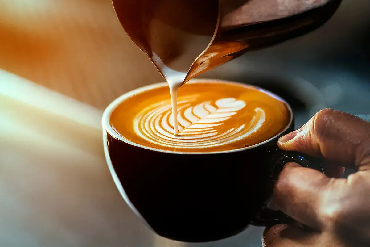 Barista gie&szlig;t cremige **cappuccino milch** in eine Tasse, um ein Latte Art Muster zu kreieren.