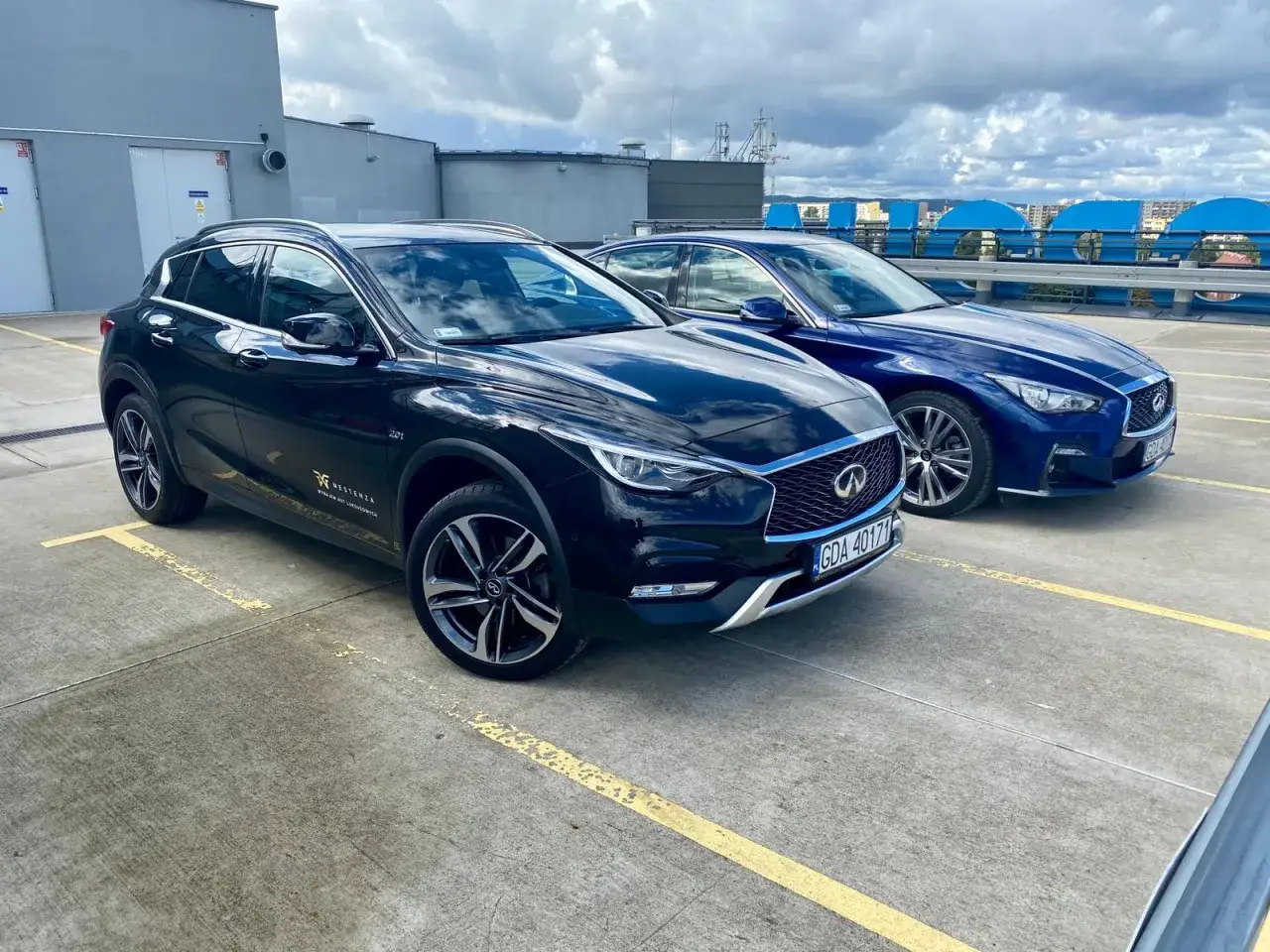 Dwa lśniące Infiniti, czarny QX30 i niebieski sedan, zaparkowane na dachu.