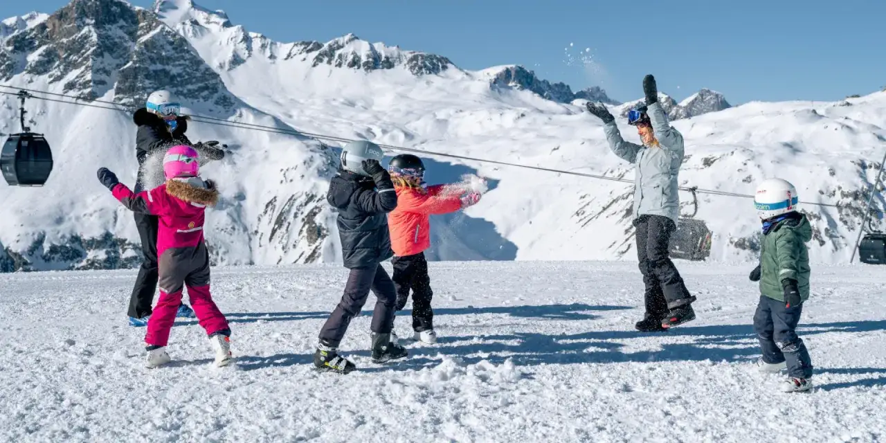 Famille s'amusant dans la neige, profitant des sports d'hiver avec des montagnes enneigées en arrière-plan.