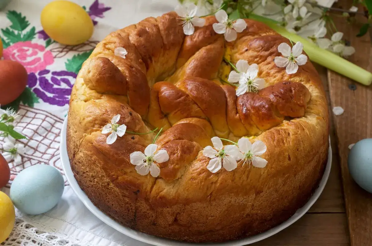 Puszyste ciasto drożdżowe z serem, ozdobione wiosennymi kwiatami i kolorowymi jajkami, zapowiada wielkanocne świętowanie.