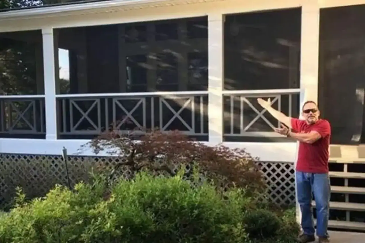 Man proudly shows off his newly screened-in porch, a perfect example of how to screen in a porch for bug-free relaxation.