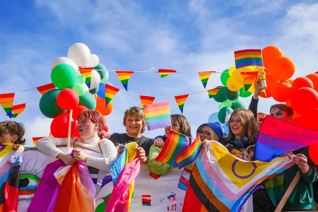 Joyful crowd at gay Reykjavik Pride, waving rainbow flags and balloons under a blue sky.