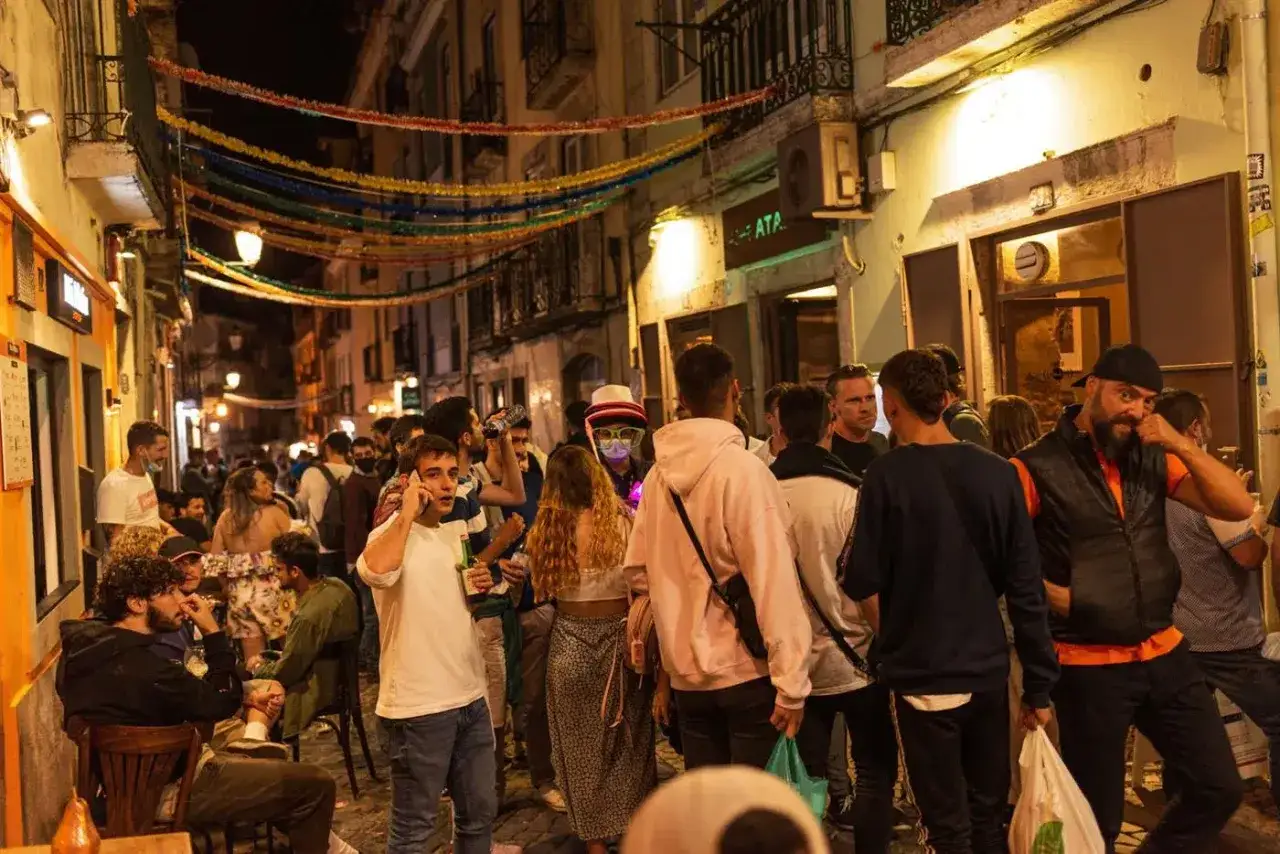 Menschen genie&szlig;en die Nacht in Lissabon. Bunte Girlanden schm&uuml;cken die Gasse, w&auml;hrend sich die Menge vor den **Lissabon Clubs** versammelt.