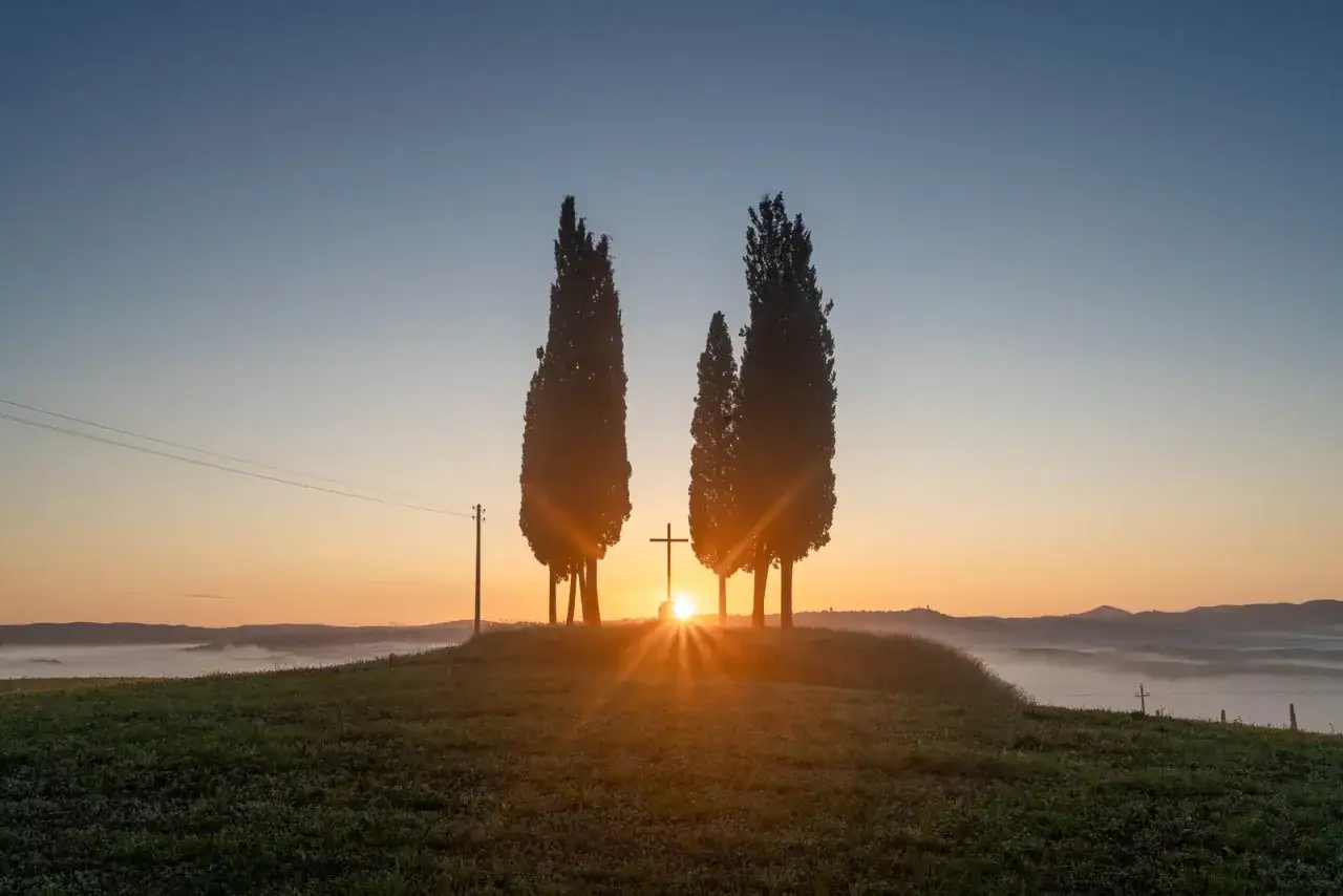 Alba in Toscana con cipressi, croce e un suggestivo effetto HDR. La nebbia avvolge le colline.