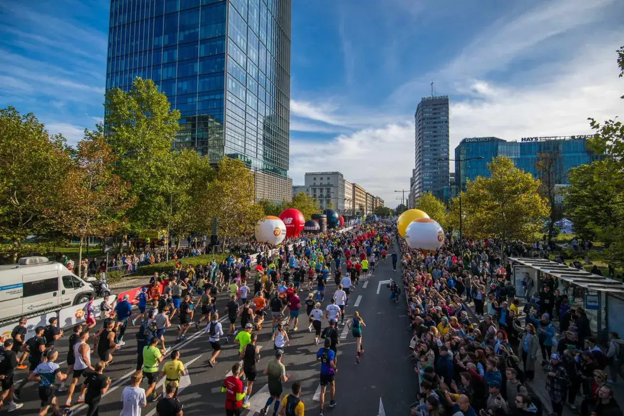 Tłum kibic&oacute;w na ulicach Warszawy podczas jednego z największych bieg&oacute;w w Polsce. Wielkie balony unoszą się nad trasą maratonu.