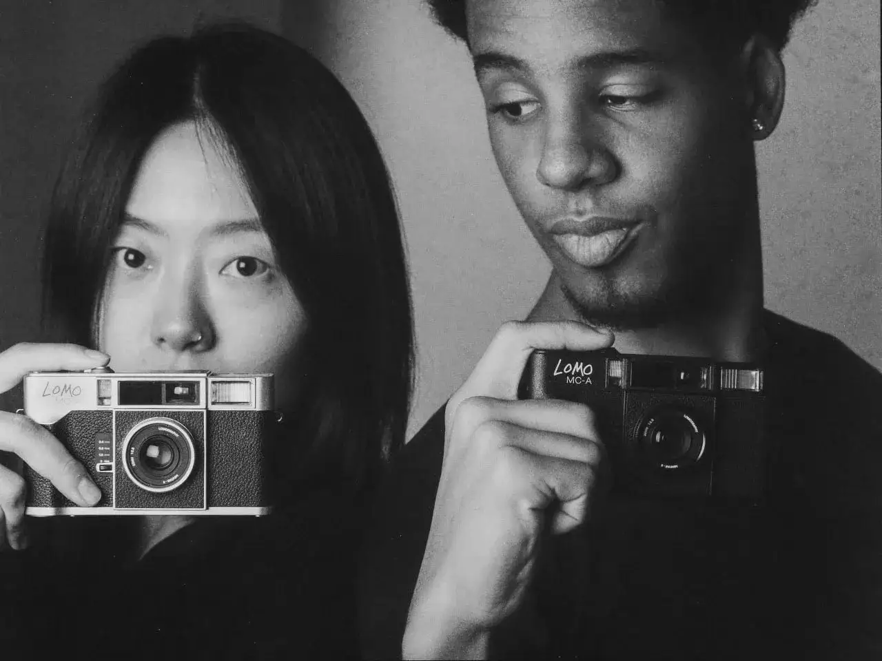 Dos jóvenes sostienen cámaras digitales analógicas Lomo, listos para capturar momentos.