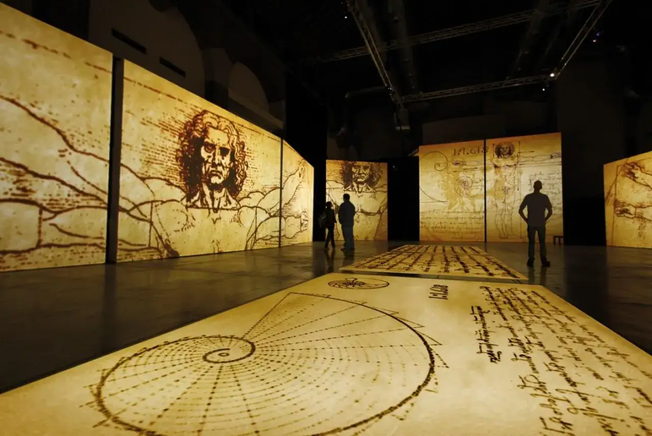 Wystawa prezentująca szkice i rysunki z **leonardo da vinci biografia**. Ludzie oglądają projekcje dzieł mistrza.