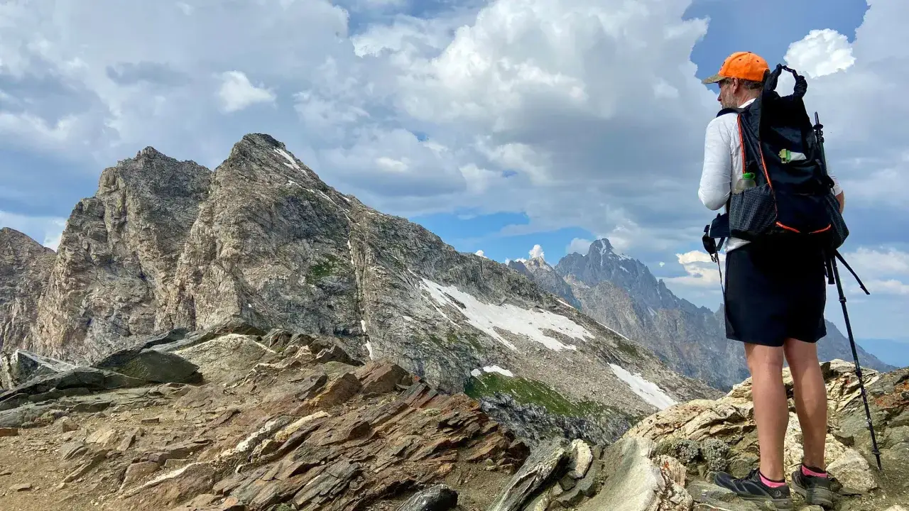 Osoba z plecakiem i kijami trekkingowymi podziwia majestatyczne g&oacute;ry. To właśnie jest hiking &ndash; przygoda na szlaku!