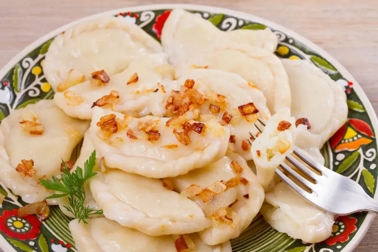 Pyszne pierogi ruskie z farszem Magdy Gessler, posypane skwarkami, na ozdobnym talerzu.
